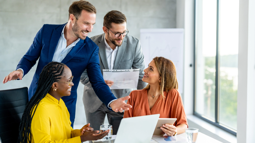 A happy meeting of three agents and one client review important information on several documents and computers